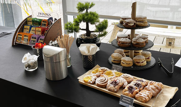 A table filled with pastries, tea and coffee, plates, and other serveware items.